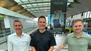 Guido Miletic, Michael Dyllong und Sonnhard Osyka posieren vor einem Banner für das Pop-up-Restaurant von Michael Dyllong am Flughafen