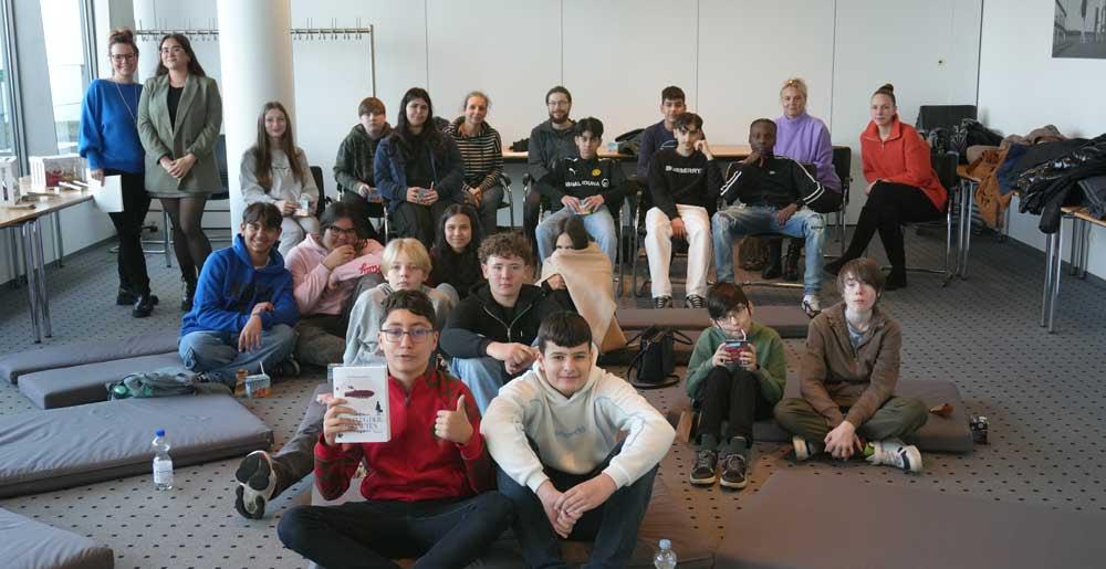 17 Siebtklässlerinnen und Siebtklässler der Hauptschule Scharnhorst lauschen am Flughafen Dortmundeiner spannenden Geschichte rund ums Fliegen