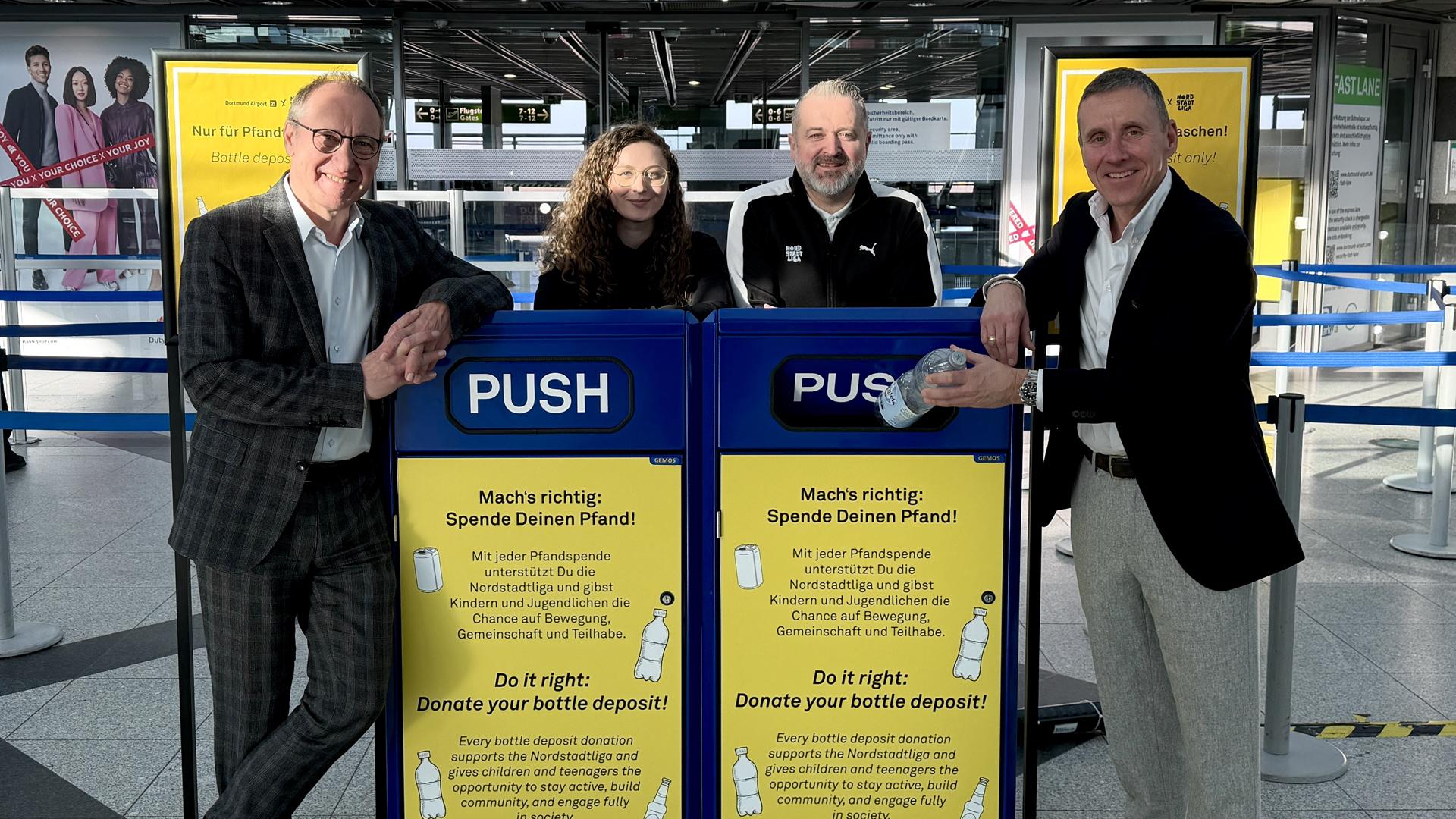 Ludger van Bebber (Geschäftsführer Dortmund Airport), Henrike Deitert (Nordtstadtliga Queens), Mirza Demirović (Head of Nordstadtliga)und Guido Miletic (Leiter Airport Services + Marketing & Sales) stehen hinter einer der neuen Sammelboxen für die Pfandspenden