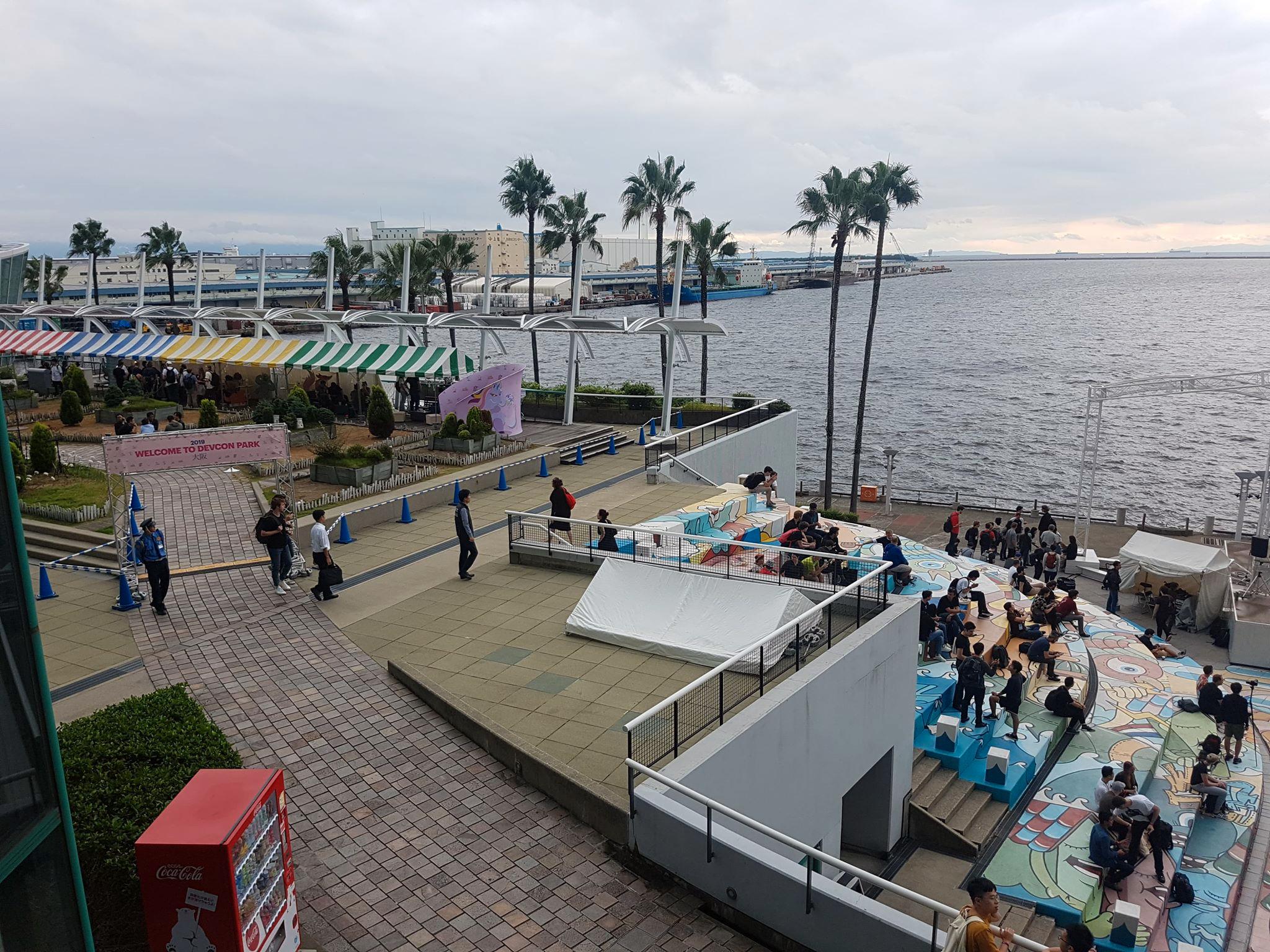 People gathered on a palm-lined waterfront terrace.