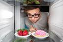 ein mann schaut in einem kühlschrank auf obst und süßes 