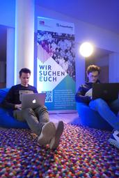 zwei Männer sitzen mit Laptop auf den Knieen auf dem Boden