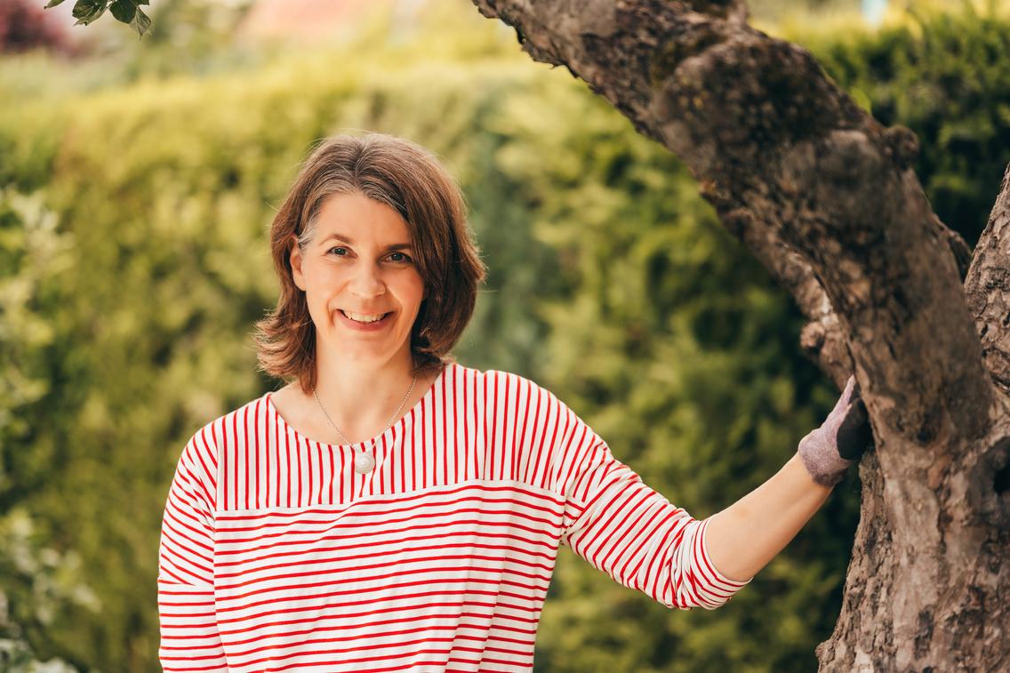 Frau lehnt lächelnd an einen Baum