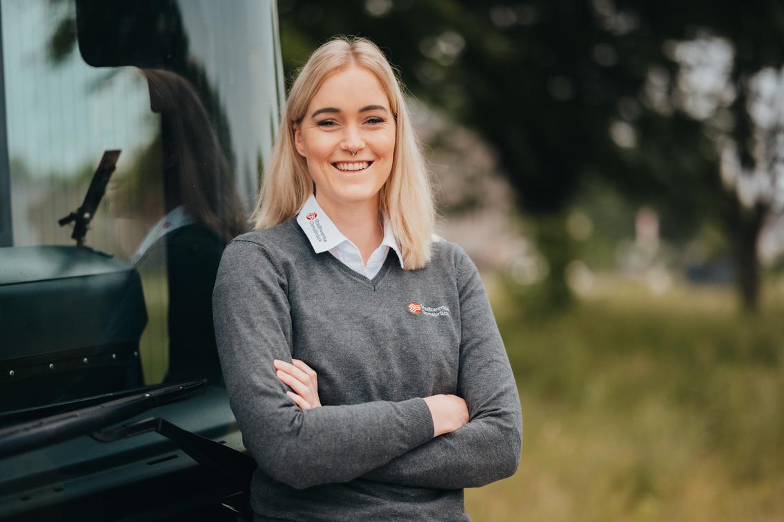 Frau steht lachend vor einem Bus