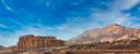 Der Totentempel der Hatschepsut in Deir el-Bahari, Ägypten, vor einer Kulisse aus felsigen Bergen und blauem Himmel. Die mehrstöckige Tempelanlage mit Säulenreihen zeigt Spuren des Verfalls und ist ein Beispiel altägyptischer Architektur.