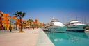 Marina in Hurghada mit Yachten, Promenade, Palmen und bunten Gebäuden bei klarem Himmel.