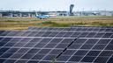 Große Photovoltaikanlage mit über 22.000 Solarmodulen im Vordergrund, dahinter der Airport Nürnberg mit Flugzeugen, Rollbahnen und Tower bei klarem Himmel.