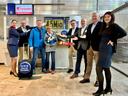 Group photo at Nuremberg Airport in front of the Corendon Priority Check-in. A group of employees and a couple of travellers stand together smiling. The person in the centre is holding a bouquet of flowers, next to which a model aeroplane from Corendon is displayed. In the foreground is a black suitcase with the words “Lucky we have it” printed on it. Departure boards can be seen in the background.