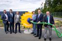 Sechs Männer in Businesskleidung stehen neben einem gelben Zahnrad mit der Aufschrift „100 PROZENT SONNENSTROM“ vor einer großen Solaranlage und halten einen grünen Schlauch.
