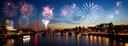 Farbenfrohes Feuerwerk über einer Stadtlandschaft bei Dämmerung, mit Spiegelungen im Wasser. Zu sehen sind der London Eye und beleuchtete Gebäude entlang des Flussufers, die eine festliche Stimmung erzeugen.