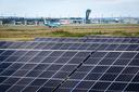 Große Photovoltaikanlage mit über 22.000 Solarmodulen im Vordergrund, dahinter der Airport Nürnberg mit Flugzeugen, Rollbahnen und Tower bei klarem Himmel.