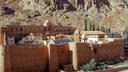 Das Katharinenkloster am Fuße des Berges Sinai in Ägypten, umgeben von massiven Steinmauern. Die Klostergebäude haben rote Dächer und weiße Wände, im Hintergrund ragen felsige Berge empor.