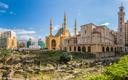 Die Mohammad-Al-Amin-Moschee in Beirut mit großem blauen Kuppeldach und vier Minaretten, im Vordergrund antike Ruinen mit Steinstrukturen und Grünflächen, umgeben von modernen Gebäuden unter klarem Himmel mit wenigen Wolken.