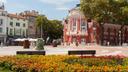 Zentraler Platz in Varna mit dem historischen Theatergebäude, umgeben von grünen Bäumen, bunten Blumenbeeten und umliegenden Häusern bei sonnigem Wetter.