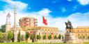 Stadtansicht von Tirana, Albanien: Zu sehen sind ein Uhrturm, ein Minarett, das historische Gebäude mit gelben und roten Akzenten sowie die albanische Flagge. Rechts im Bild steht das Reiterstandbild von Skanderbeg vor einem klaren Himmel.