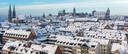 Winterliche Stadtansicht von Nürnberg mit schneebedeckten Dächern, der Kaiserburg im Hintergrund und klarem blauem Himmel.