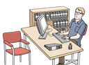 Ein blonder Mann mit einer Brille sitzt an einem Schreibtisch, auf dem ein Computer steht. Hinter ihm steht ein Regal mit Ordnern. Auf der anderen Seite des Tisches steht ein roter Stuhl.