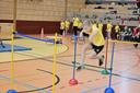 Ein Kind springt in einer Turnhalle über ein Hindernis. Im Hintergrund sitzen weitere Kinder und schauen zu.