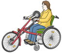 Eine Frau sitzt in ihrem Rollstuhl. Vor ihr steht ein Rad, dass sie durch Pedale mit den Händen bewegen kann. So fährt die Frau Fahrrad. Die hat braune Haare, trägt einen gelben Pullover und eine blaue Hose.