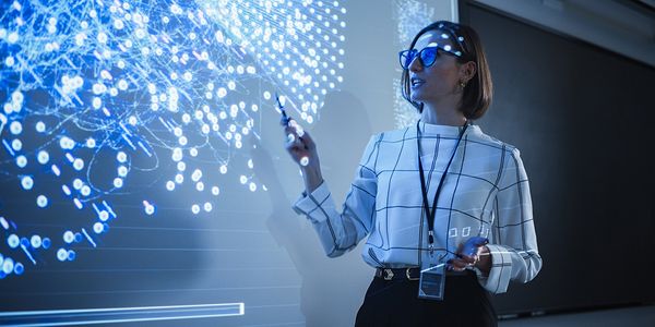 Das Bild zeigt eine Frau, die auf eine Projektion links von ihr zeigt. Die Projektion zeigt ein Netz aus vielen kleinen blauen Punkten.