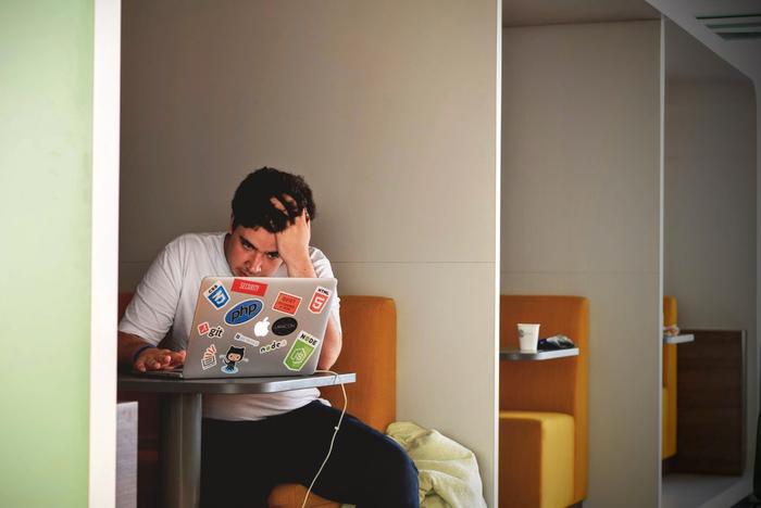 A man is sitting in front of his laptop and is looking stressed because the website is very slowly.
